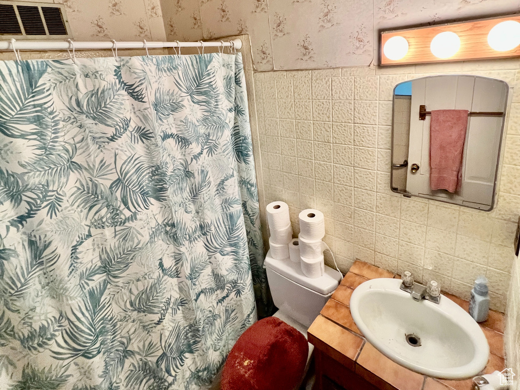 Bathroom featuring tile walls, toilet, and vanity with extensive cabinet space