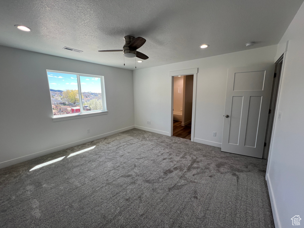 Unfurnished bedroom with ceiling fan, dark colored carpet, a textured ceiling, and connected bathroom