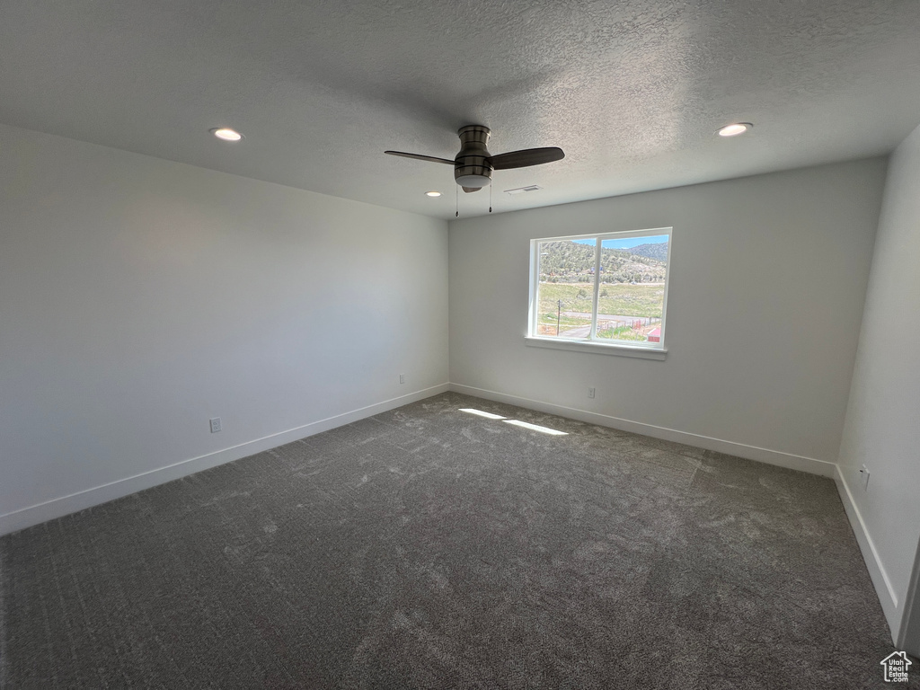 Unfurnished room with ceiling fan, dark colored carpet, and a textured ceiling