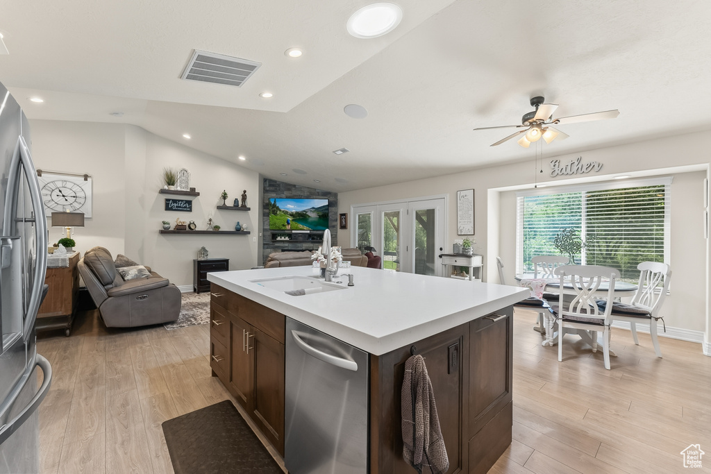 Kitchen featuring stainless steel appliances, vaulted ceiling, a kitchen island with sink, and light wood-type flooring