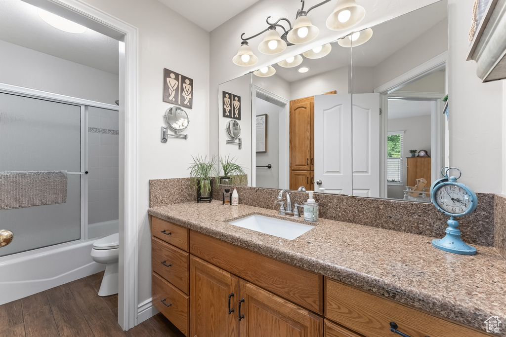 Full bathroom with hardwood / wood-style floors, vanity, toilet, and bath / shower combo with glass door