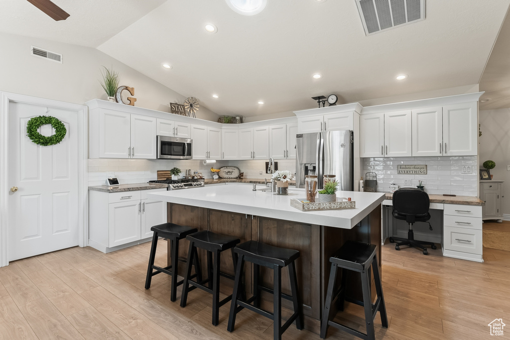 Kitchen featuring lofted ceiling, light hardwood / wood-style flooring, stainless steel appliances, white cabinets, and tasteful backsplash