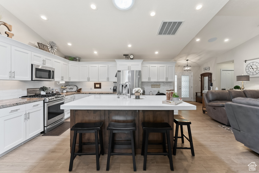 Kitchen featuring appliances with stainless steel finishes, light hardwood / wood-style floors, an island with sink, and a breakfast bar