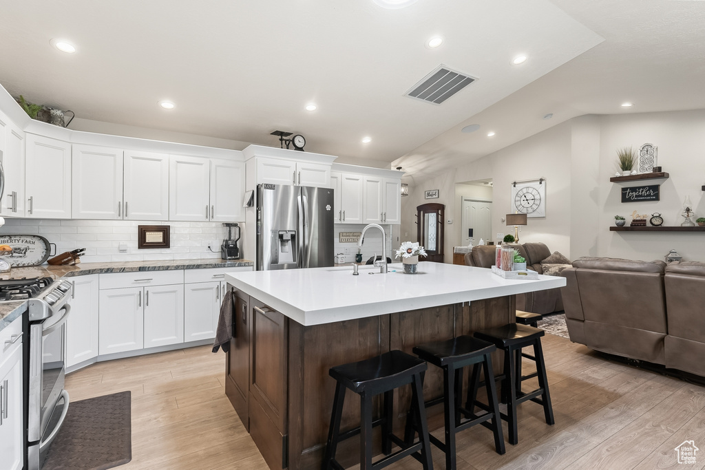 Kitchen featuring light hardwood / wood-style floors, a kitchen island with sink, range with gas cooktop, backsplash, and stainless steel refrigerator with ice dispenser