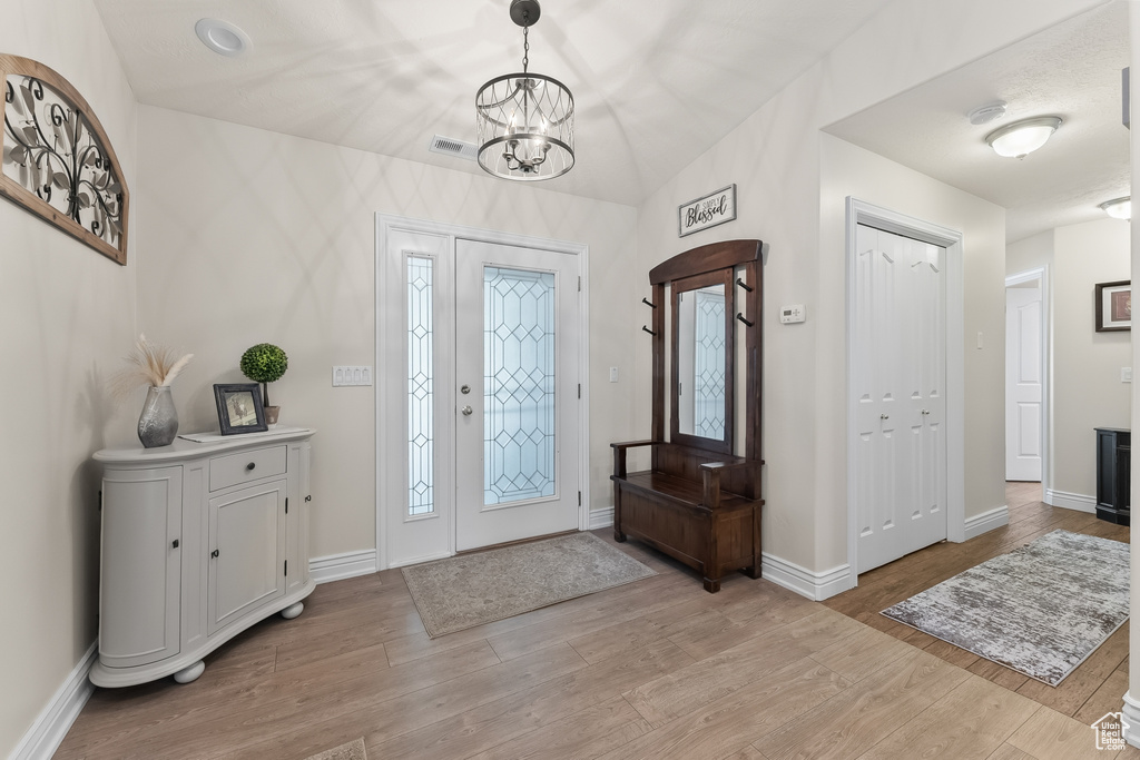 Entryway with light hardwood / wood-style floors, a chandelier, and vaulted ceiling