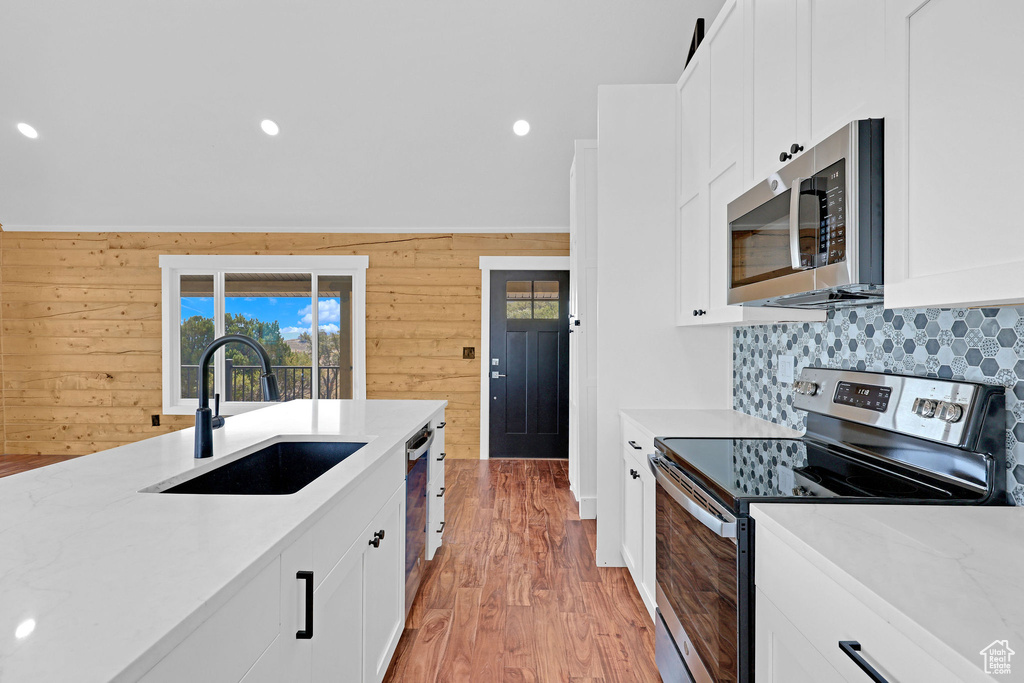 Kitchen featuring wood walls, sink, tasteful backsplash, appliances with stainless steel finishes, and light stone countertops