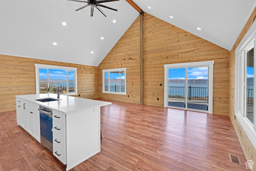 Kitchen featuring light hardwood / wood-style floors, white cabinets, wood walls, a center island with sink, and sink