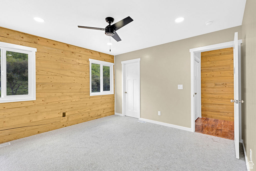 Unfurnished bedroom featuring carpet flooring, wooden walls, multiple windows, and ceiling fan