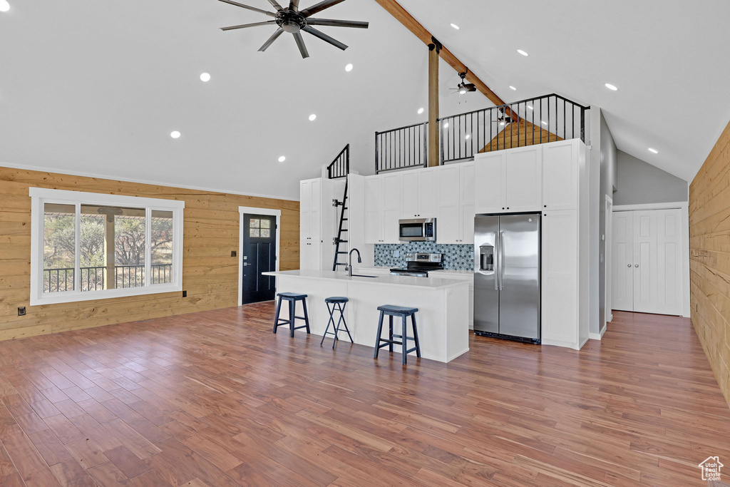 Kitchen with a kitchen bar, wood walls, a center island with sink, and appliances with stainless steel finishes