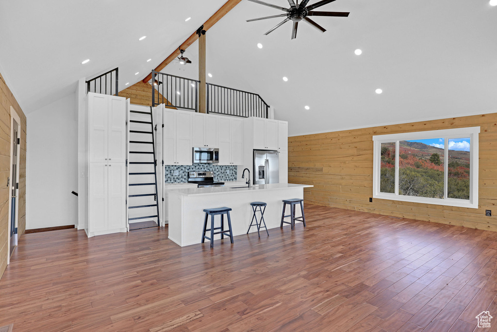 Kitchen with a large island with sink, a breakfast bar area, stainless steel appliances, wooden walls, and ceiling fan