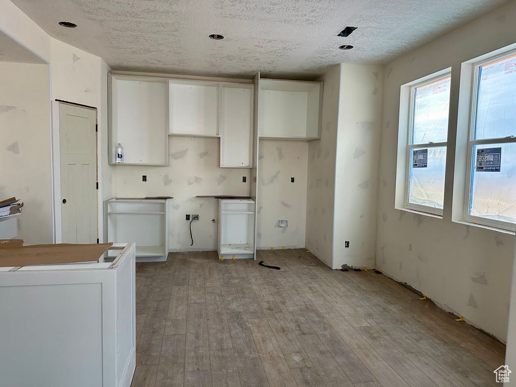 Kitchen with white cabinetry, light hardwood / wood-style floors, and a textured ceiling