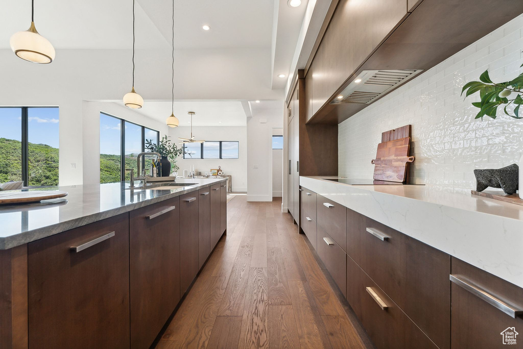 Kitchen with hanging light fixtures, dark hardwood / wood-style flooring, stone countertops, sink, and black electric cooktop