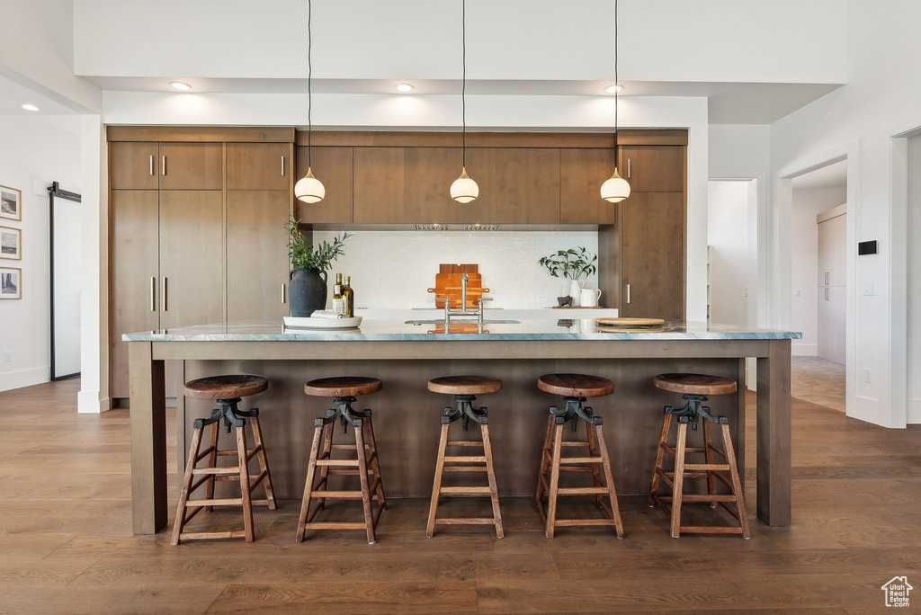 Bar with decorative light fixtures, light stone countertops, dark hardwood / wood-style flooring, and sink