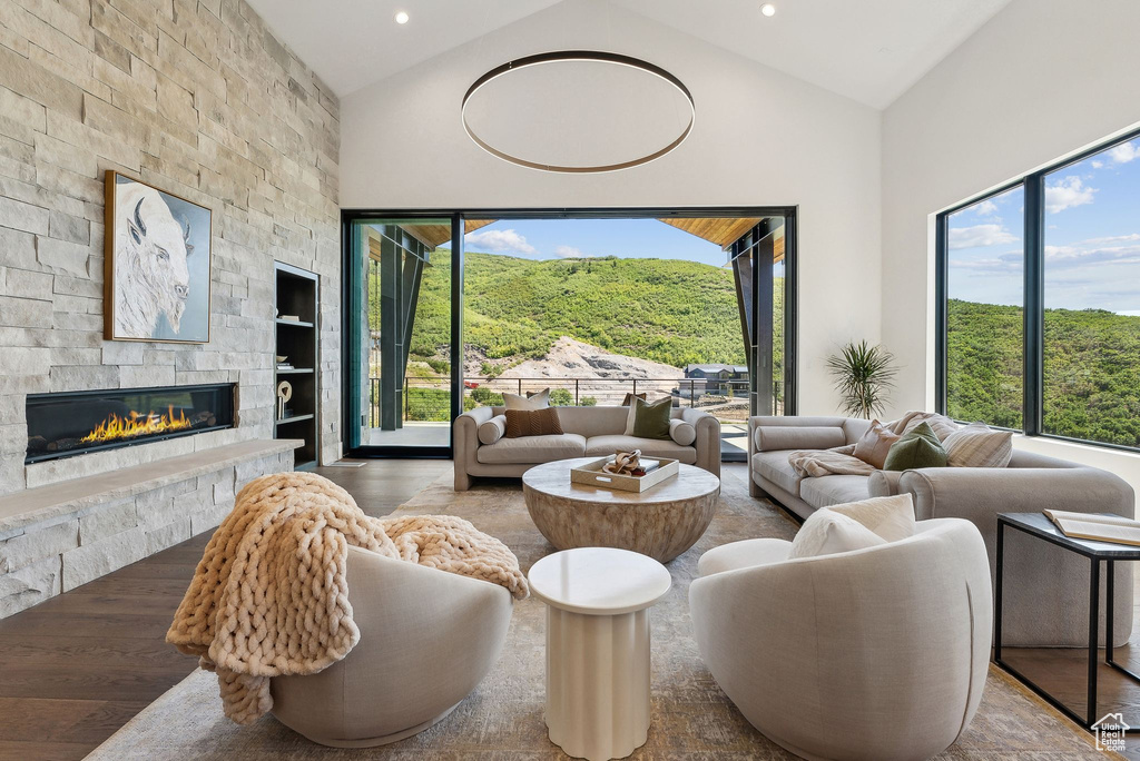 Living room with built in shelves, wood-type flooring, a stone fireplace, and high vaulted ceiling