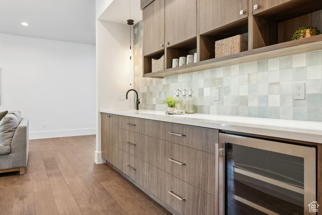 Kitchen with pendant lighting, beverage cooler, tasteful backsplash, light hardwood / wood-style floors, and sink