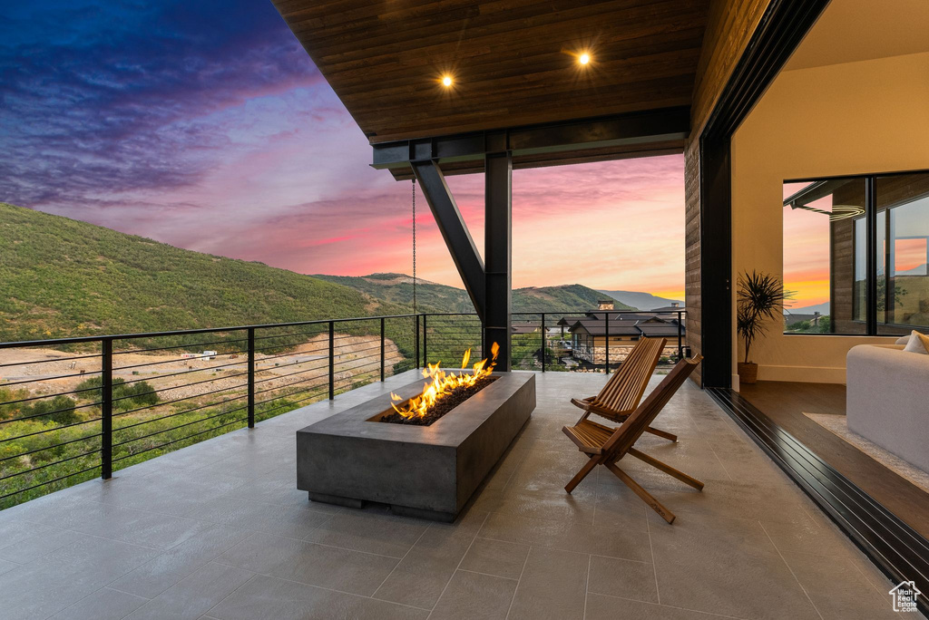 Patio terrace at dusk with a mountain view, a fire pit, and a balcony