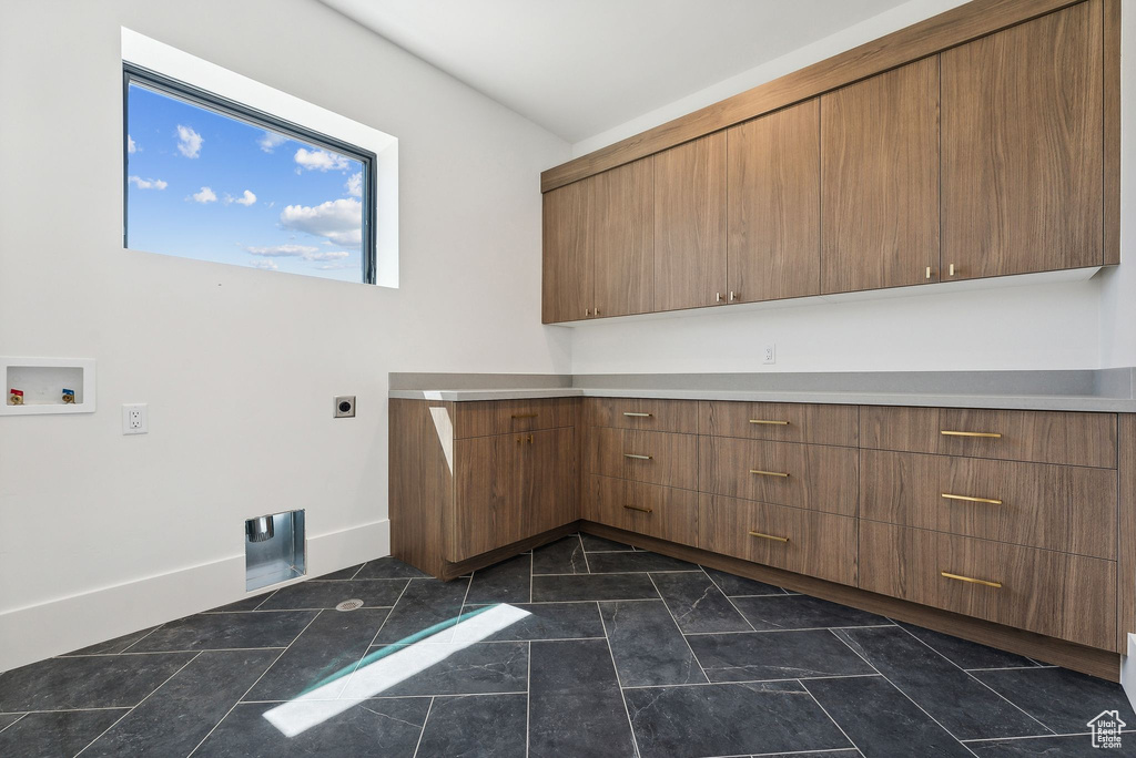 Washroom with dark tile patterned flooring, hookup for a washing machine, cabinets, and hookup for an electric dryer