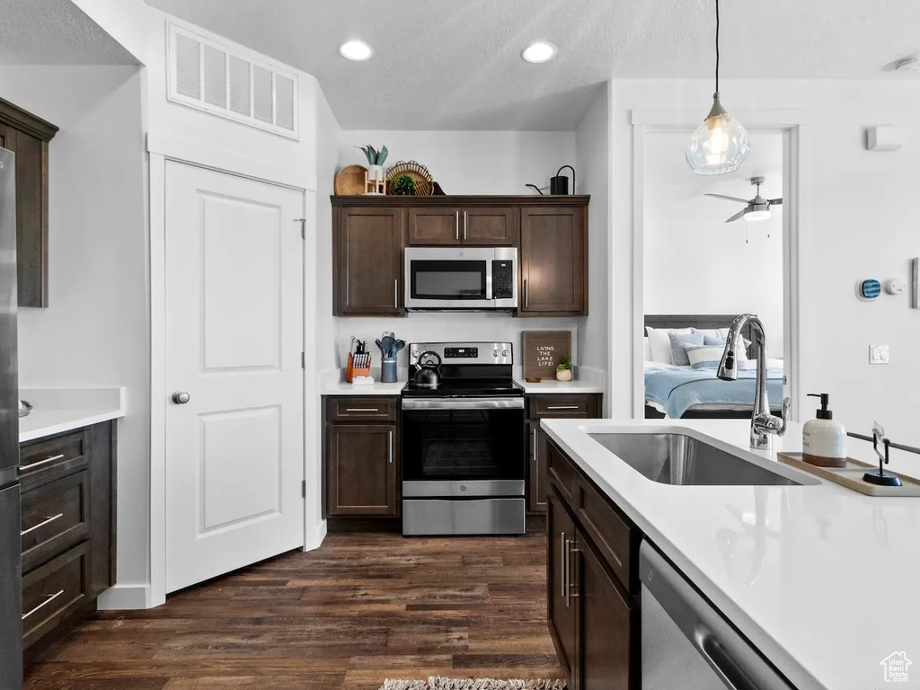 Kitchen with dark hardwood / wood-style flooring, stainless steel appliances, hanging light fixtures, ceiling fan, and sink