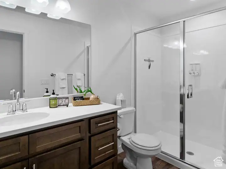 Bathroom featuring walk in shower, wood-type flooring, toilet, and vanity with extensive cabinet space