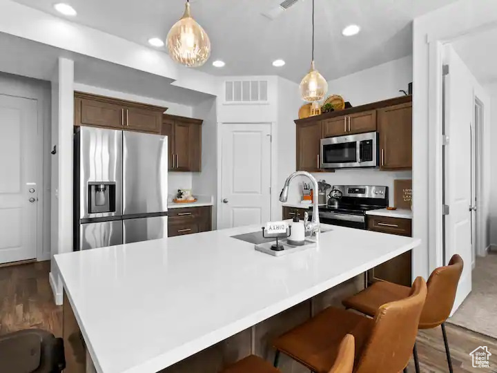 Kitchen featuring stainless steel appliances, a center island with sink, hardwood / wood-style floors, and pendant lighting