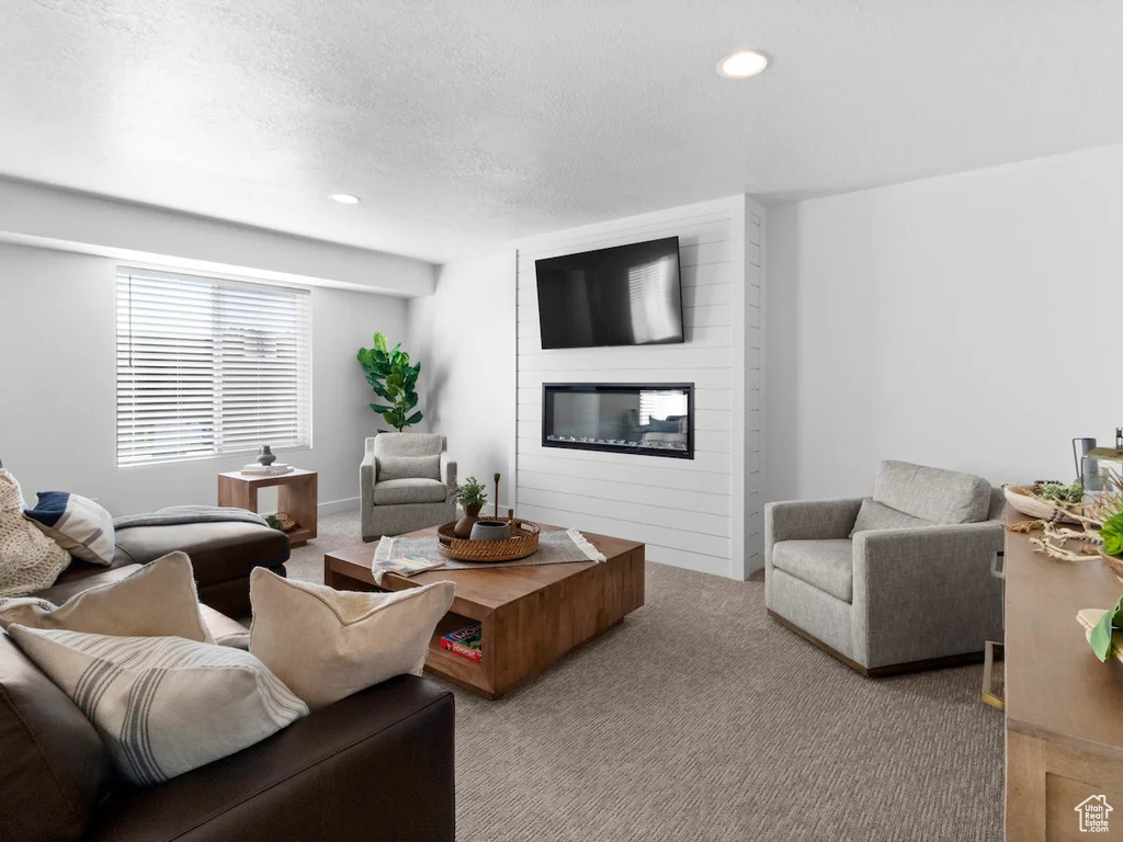 Living room featuring a large fireplace, carpet floors, a textured ceiling, and brick wall