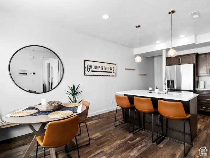 Kitchen featuring hanging light fixtures, a kitchen island with sink, stainless steel refrigerator with ice dispenser, and dark wood-type flooring