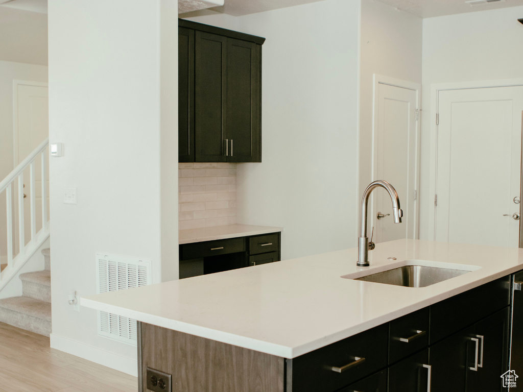 Kitchen with light hardwood / wood-style flooring, tasteful backsplash, a center island with sink, dishwashing machine, and sink