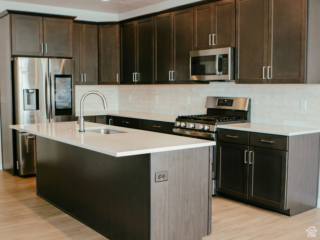 Kitchen featuring an island with sink, stainless steel appliances, light hardwood / wood-style flooring, and backsplash