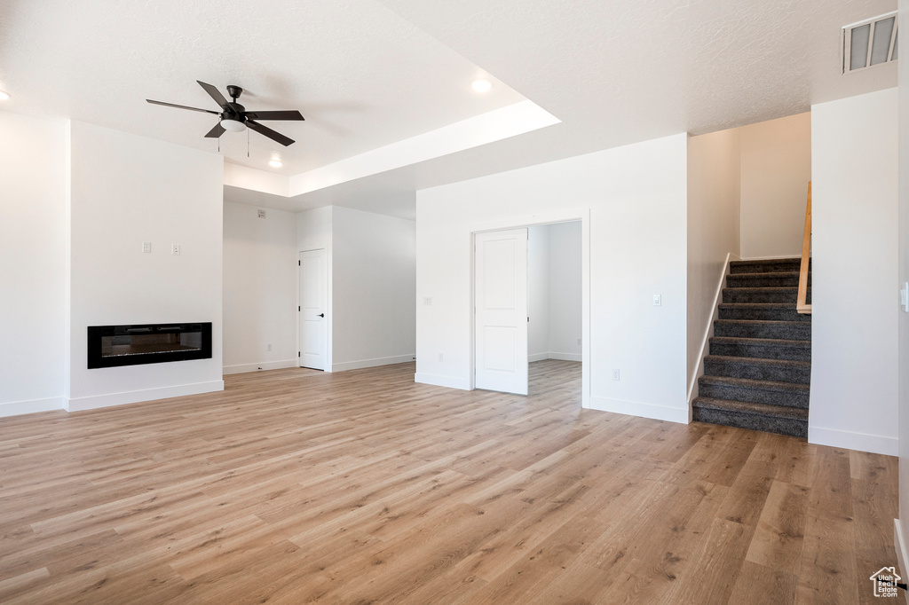 Unfurnished living room with ceiling fan, a raised ceiling, and light wood-type flooring