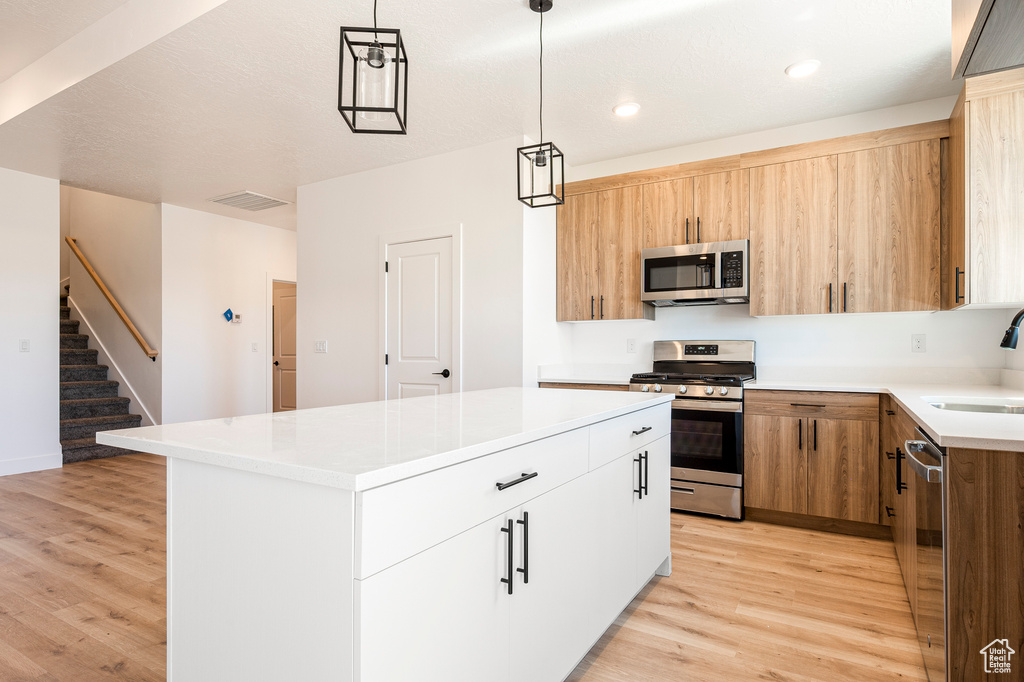 Kitchen with light wood-type flooring, white cabinets, appliances with stainless steel finishes, decorative light fixtures, and a center island