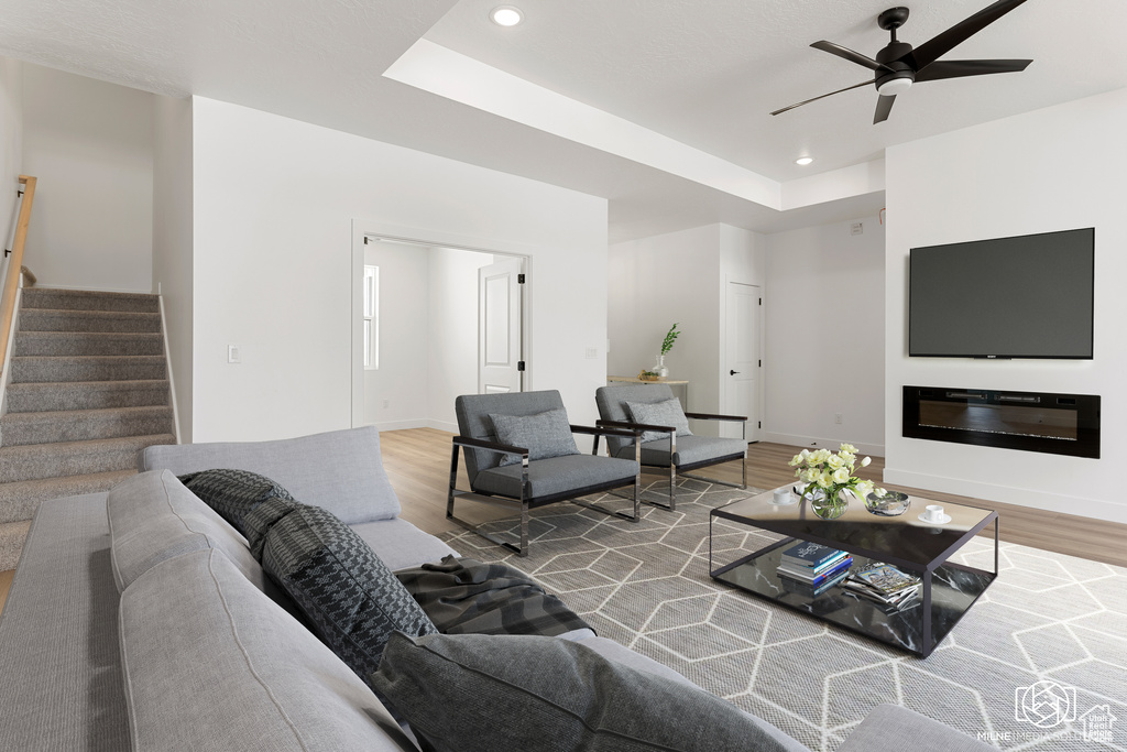 Living room with light hardwood / wood-style flooring, a tray ceiling, and ceiling fan