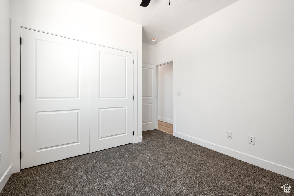 Unfurnished bedroom with ceiling fan, a closet, and dark colored carpet