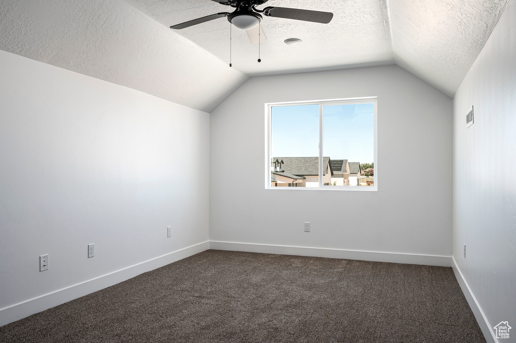 Carpeted empty room with ceiling fan, vaulted ceiling, and a textured ceiling