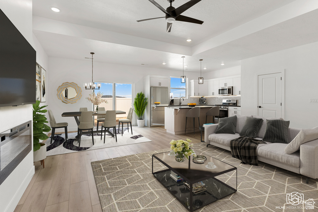 Living room with light wood-type flooring, ceiling fan with notable chandelier, and sink