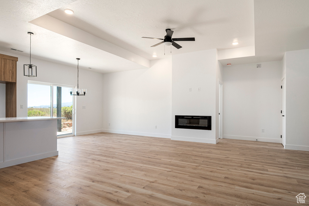 Unfurnished living room with light wood-type flooring, ceiling fan with notable chandelier, and heating unit