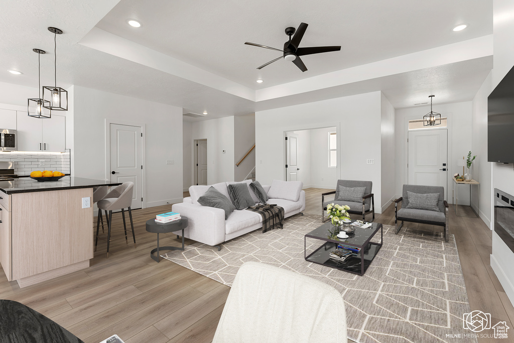 Living room featuring light wood-type flooring, ceiling fan with notable chandelier, and a tray ceiling