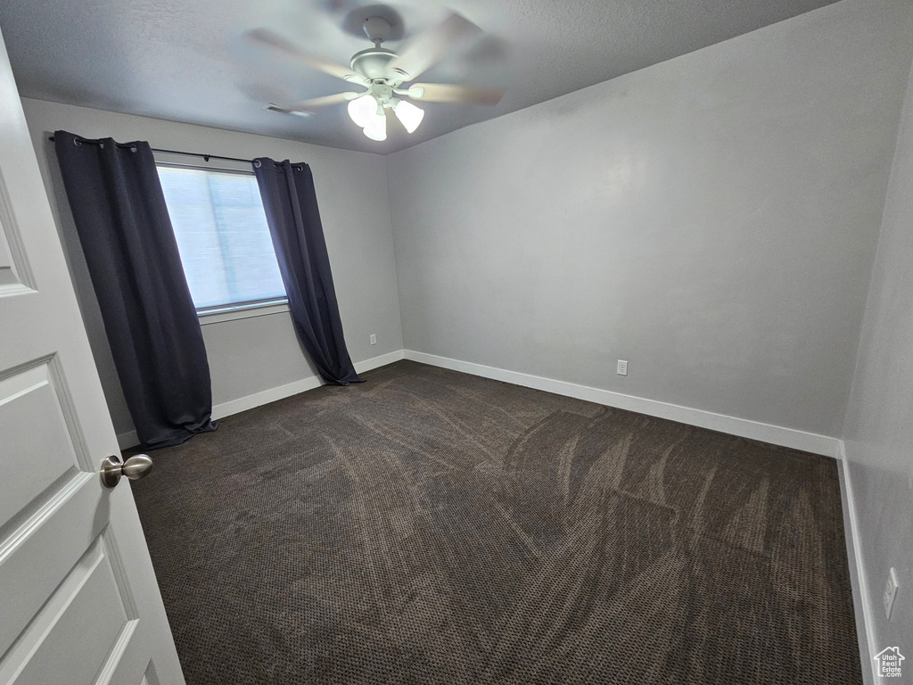 Spare room featuring ceiling fan and dark carpet