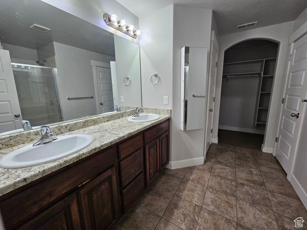 Bathroom featuring tile flooring, a textured ceiling, double sink vanity, and a shower with shower door