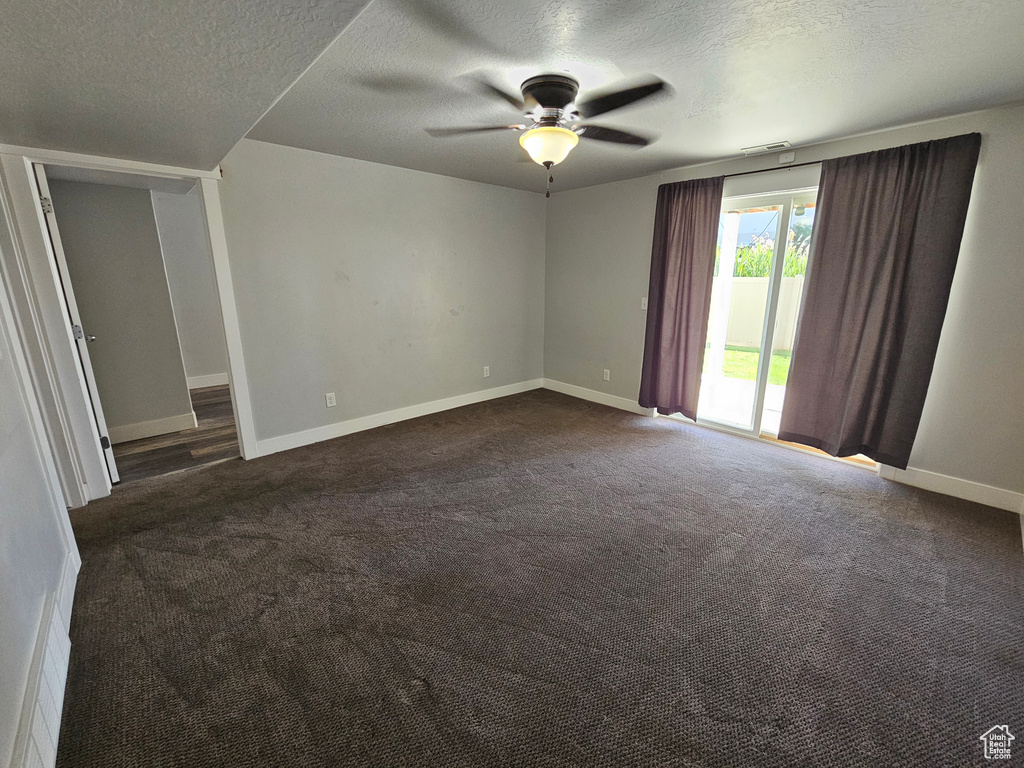 Empty room featuring dark colored carpet, ceiling fan, and a textured ceiling