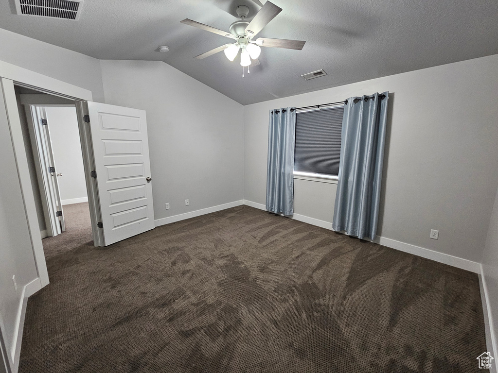 Spare room with ceiling fan, vaulted ceiling, and dark carpet