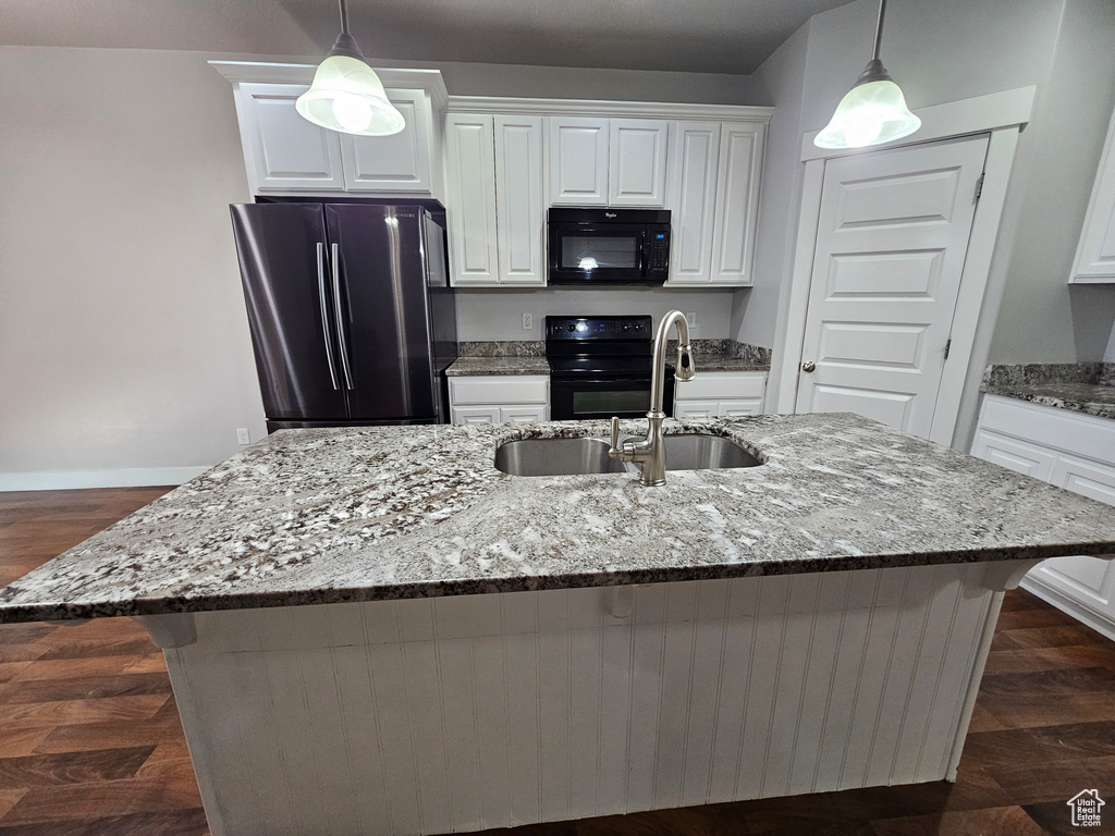 Kitchen featuring white cabinets, dark wood-type flooring, a kitchen island with sink, and refrigerator