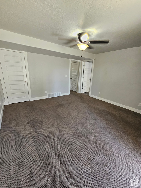 Unfurnished bedroom featuring a textured ceiling, ceiling fan, and dark carpet