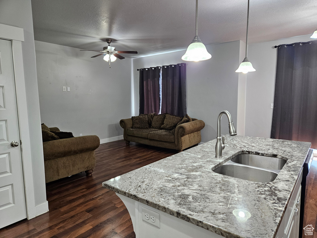 Kitchen featuring decorative light fixtures, light stone counters, ceiling fan, dark wood-type flooring, and sink