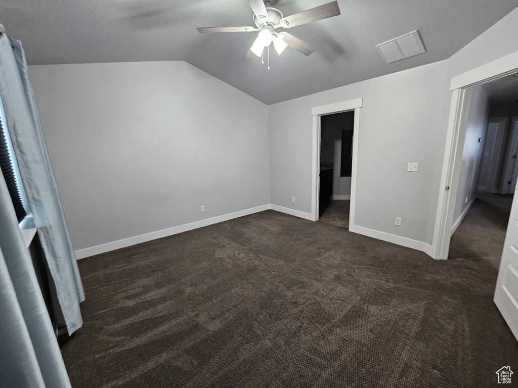 Unfurnished bedroom with dark colored carpet, ceiling fan, and vaulted ceiling