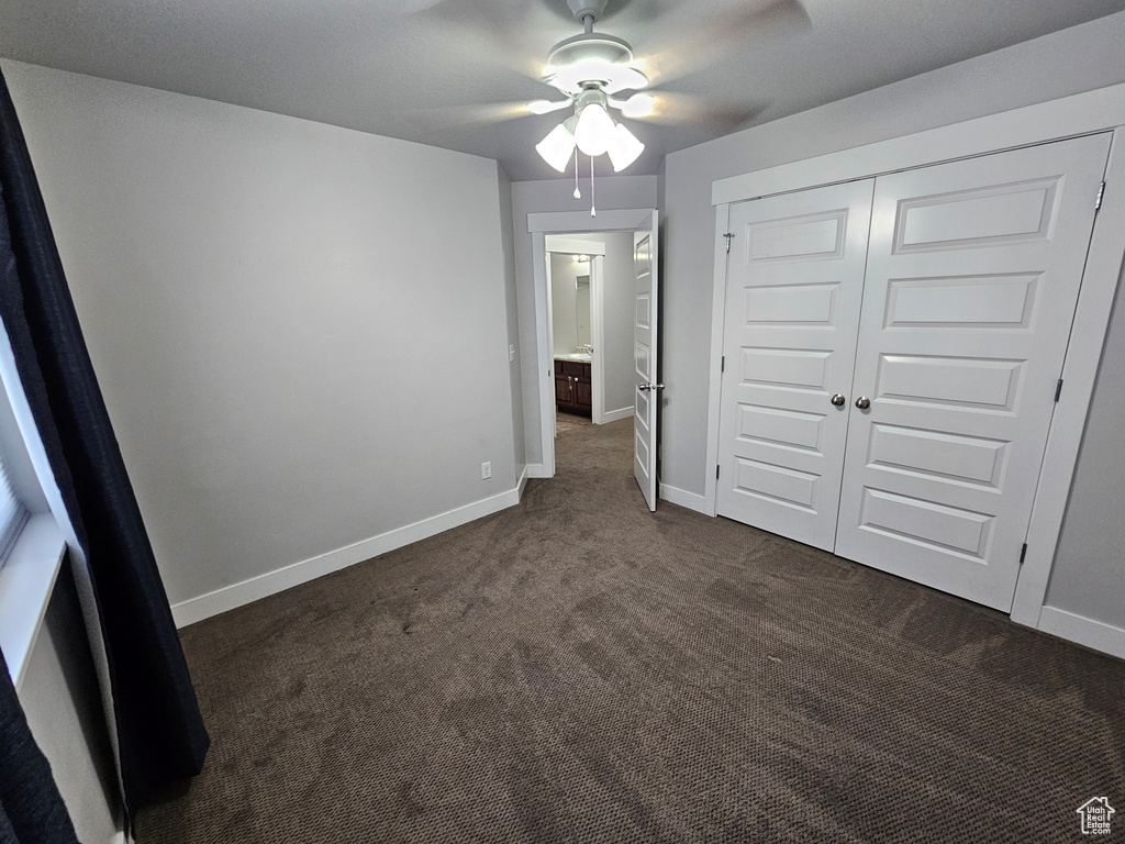 Unfurnished bedroom with ceiling fan, a closet, and dark colored carpet