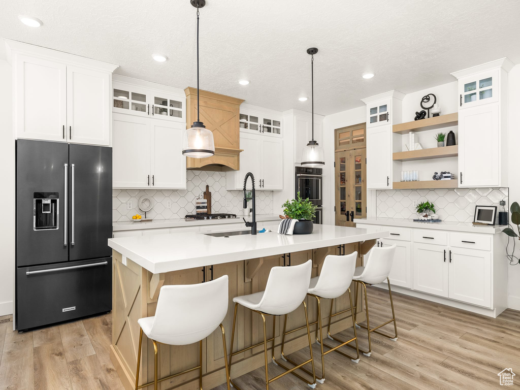 Kitchen featuring an island with sink, hanging light fixtures, tasteful backsplash, and stainless steel appliances