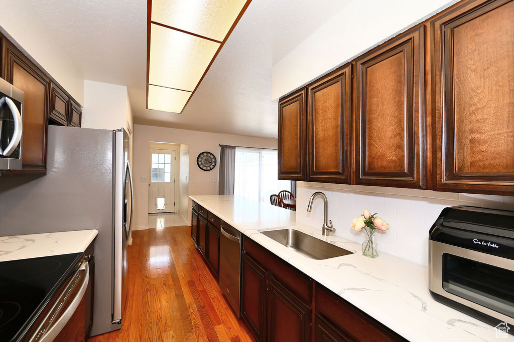 Kitchen featuring appliances with stainless steel finishes, sink, light wood-type flooring, and light stone countertops