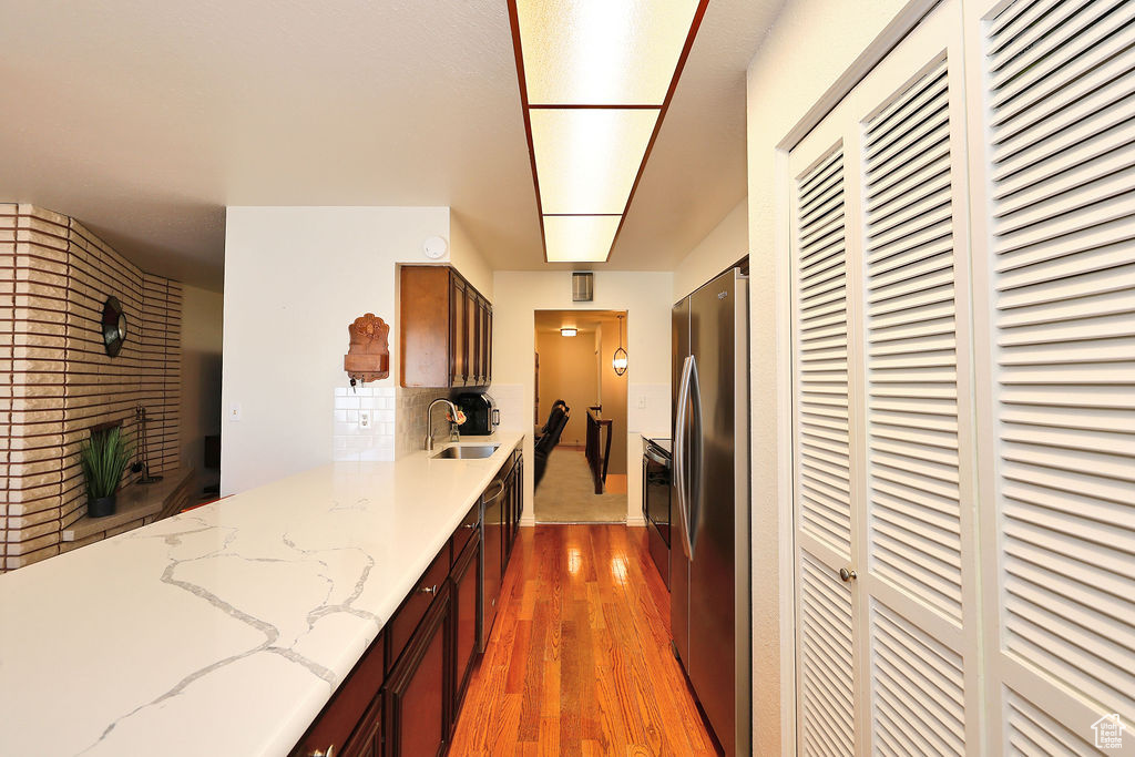 Kitchen featuring hardwood / wood-style floors, light stone counters, backsplash, sink, and appliances with stainless steel finishes