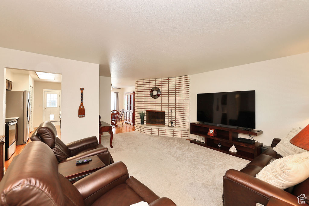 Living room featuring a textured ceiling, carpet, a large fireplace, and brick wall