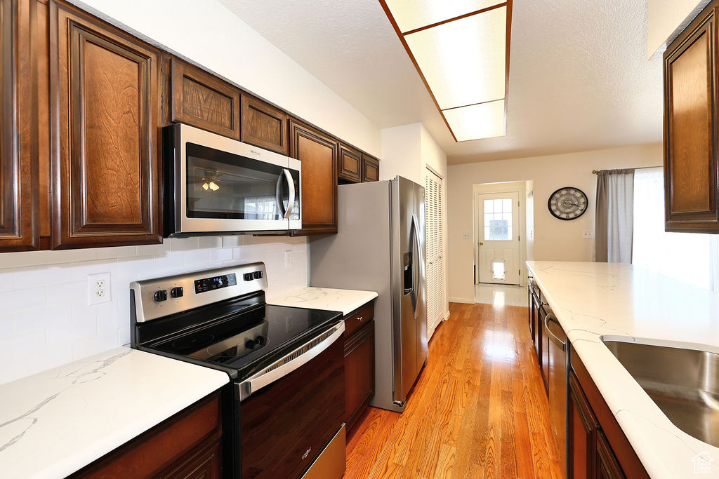 Kitchen featuring appliances with stainless steel finishes, light hardwood / wood-style floors, backsplash, and light stone counters